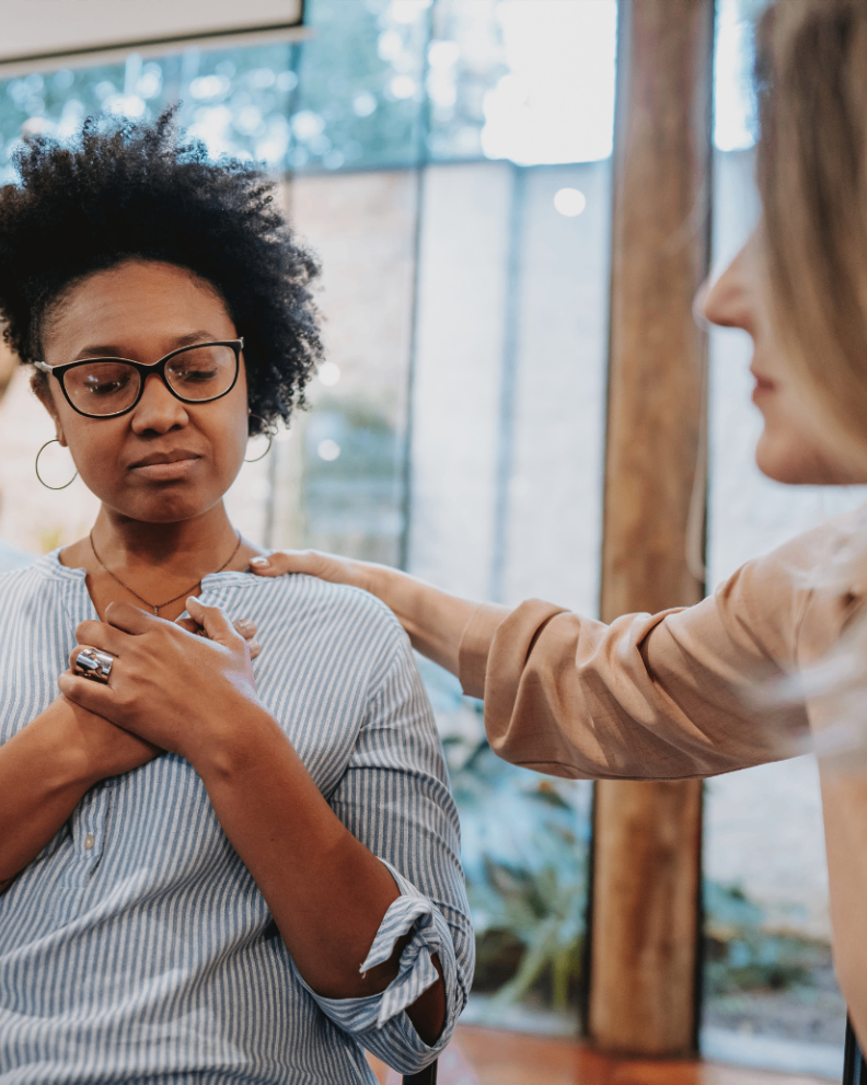 A counselor rests a supportive hand on a woman's shoulder during a one-on-one session