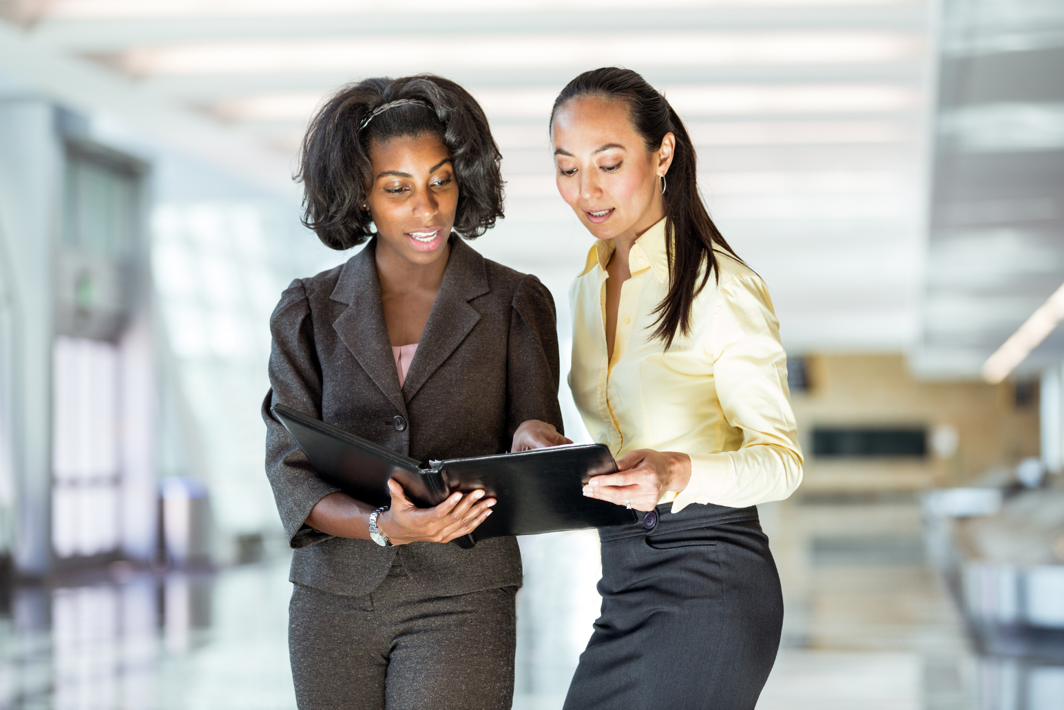 Two women in professional attire reviewing a portfolio together